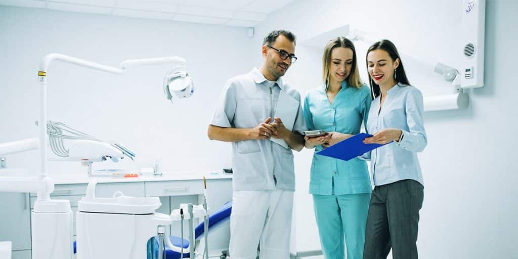 equipe de dentistas em consultório olhando tablet